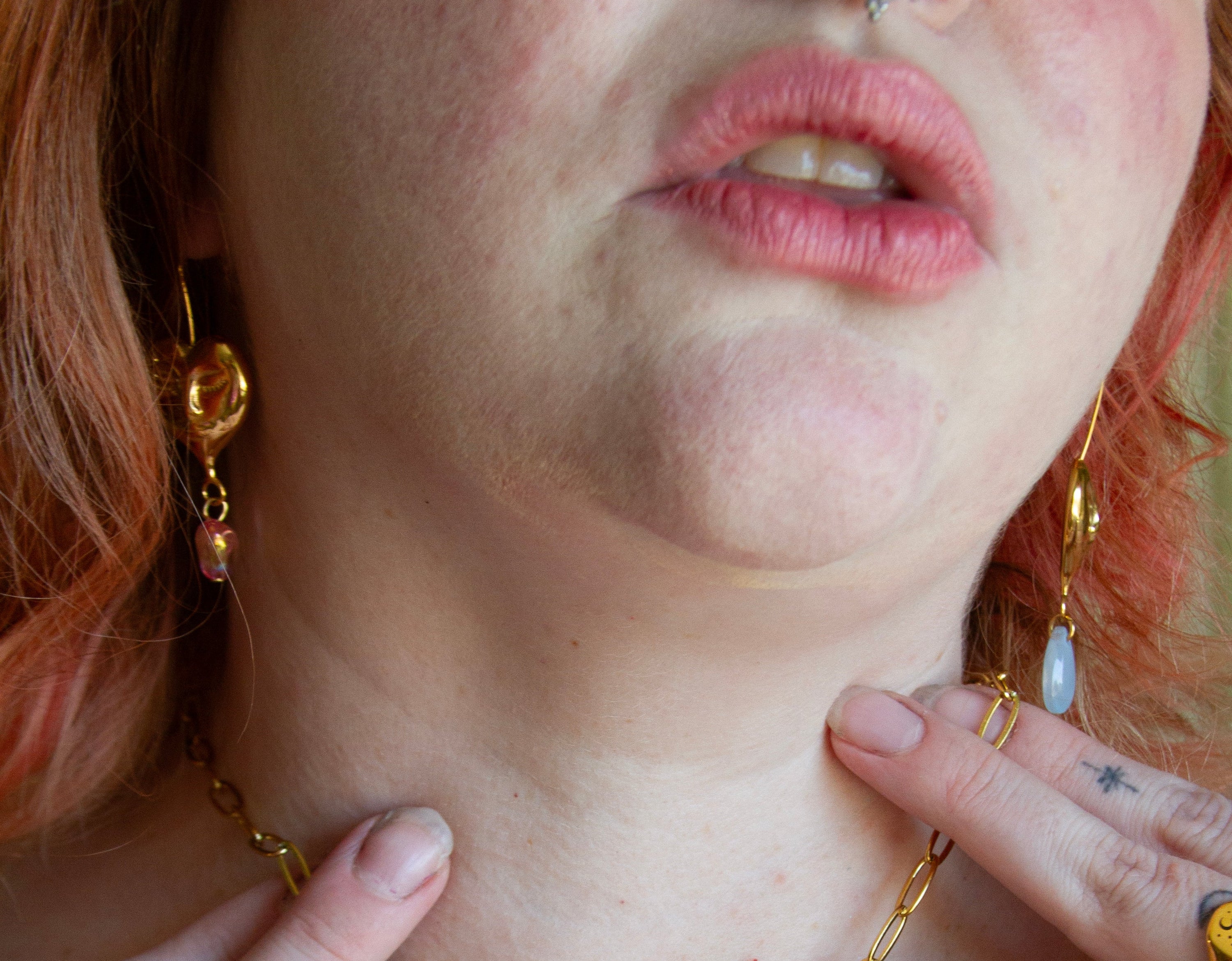 Close-up of a person wearing gold jewelry including a necklace, earrings, and rings.