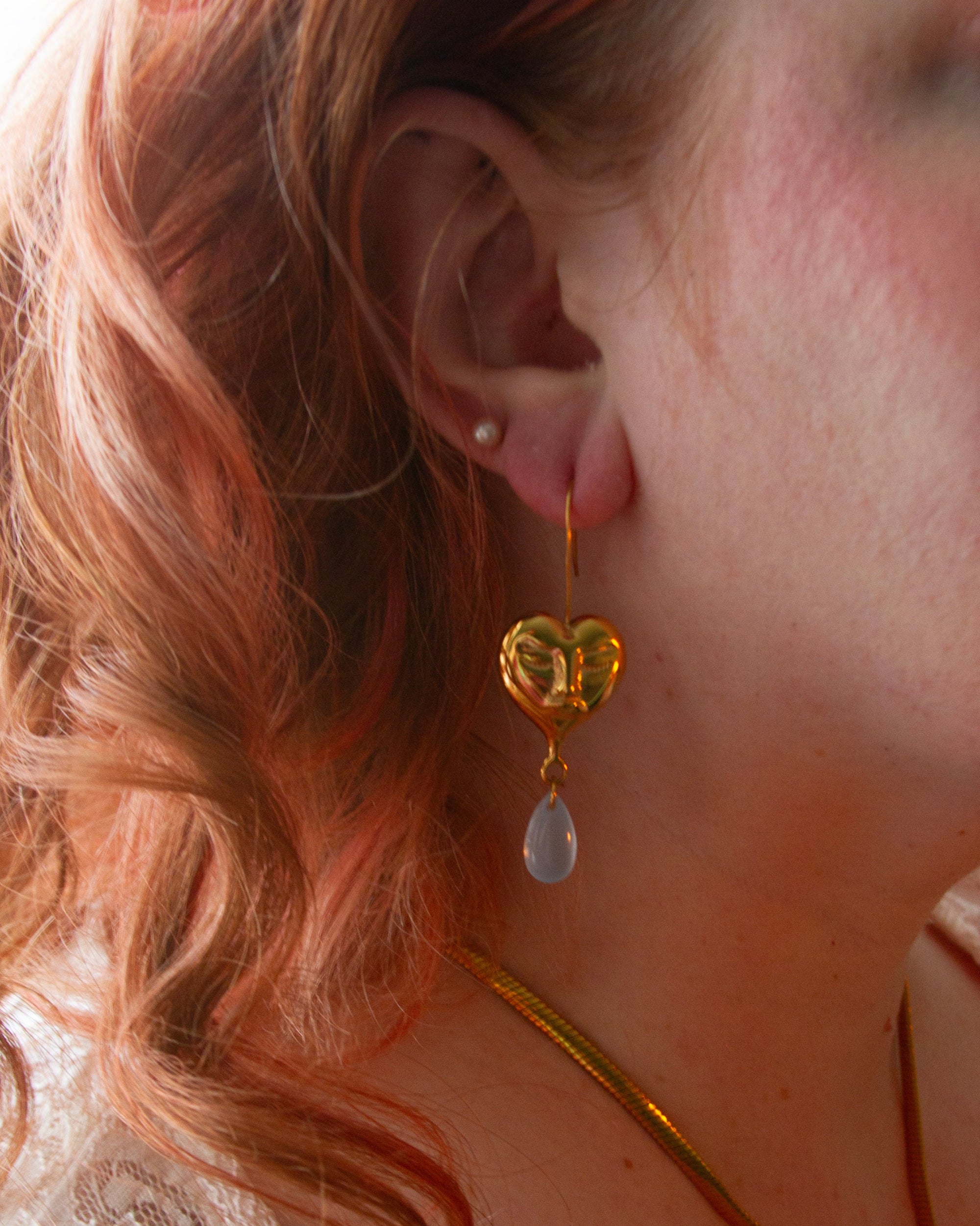 Close-up of a person wearing gold earrings with heart designs and a necklace.
